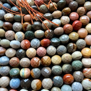 May include: A strand of faceted gemstone beads in various shades of brown, red, green, and blue. The beads are round and have a smooth, polished finish.