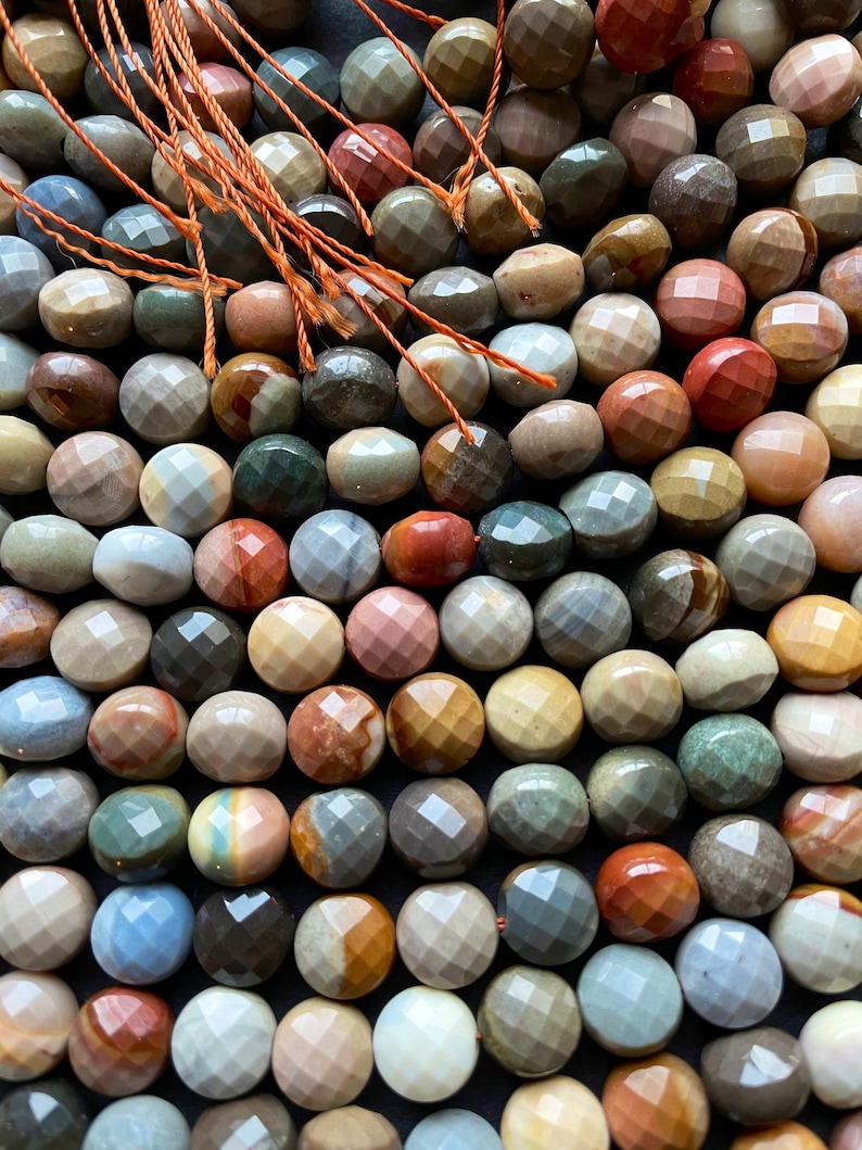 May include: A strand of faceted gemstone beads in various shades of brown, red, green, and blue. The beads are round and have a smooth, polished finish.