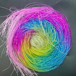 Könnte beinhalten: Eine Regenbogen-Auswahl an irisierenden Glasperlen, die in einem Kreis angeordnet sind. Die Perlen sind klein und haben eine facettierte Oberfläche, die einen schimmernden Effekt erzeugt.
