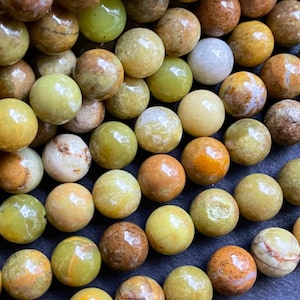 May include: A strand of round, green, yellow, and brown opal beads. The beads are smooth and polished, and they have a natural, earthy look.