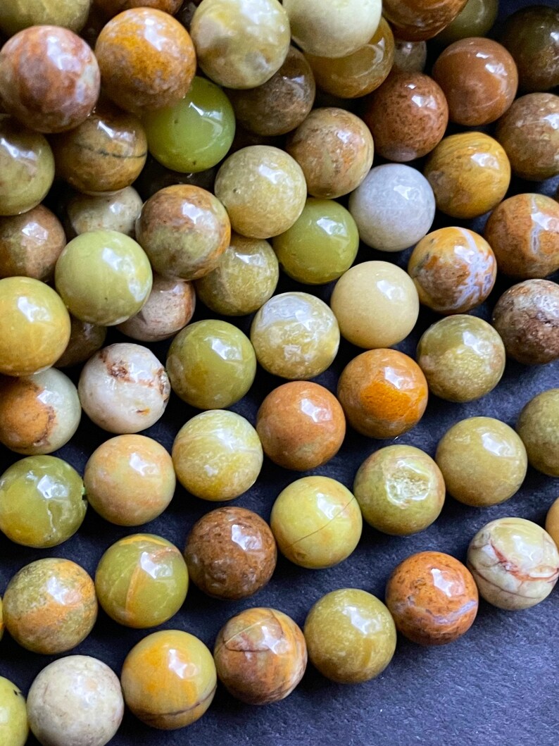 May include: A strand of round, green, yellow, and brown opal beads. The beads are smooth and polished, and they have a natural, earthy look.