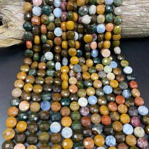 May include: A strand of multi-colored gemstone beads. The beads are round and faceted, with a variety of colors including brown, green, yellow, red, and blue. The beads are strung on a clear string.