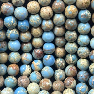 May include: A close-up of a strand of blue and brown jasper beads. The beads are round and have a mottled appearance.