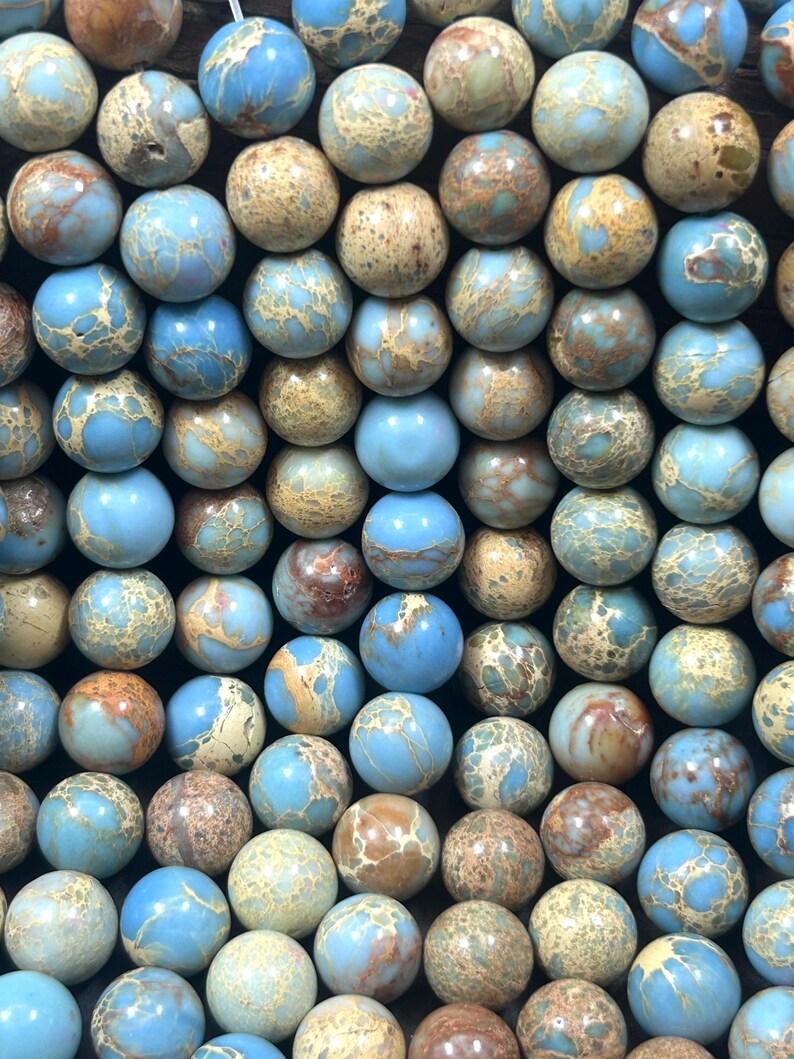 May include: A close-up of a strand of blue and brown jasper beads. The beads are round and have a mottled appearance.