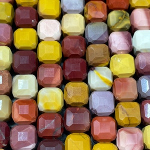 Puede incluir: Una colección de cuentas de piedras preciosas facetadas y coloridas en varios tonos de rojo, amarillo y marrón. Las cuentas están dispuestas en un patrón de cuadrícula.