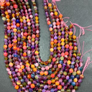 May include: A strand of multi-colored gemstone beads. The beads are round and faceted, and they are strung on a pink thread. The beads are a mix of pink, purple, orange, yellow, and green.