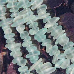 May include: A strand of light blue sea glass beads, strung on wire, with a frosted finish. The beads are arranged in a cascading pattern, creating a delicate and elegant look.