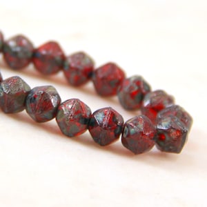 May include: A strand of red glass beads with a speckled, iridescent finish. The beads are faceted and have a slightly irregular shape.