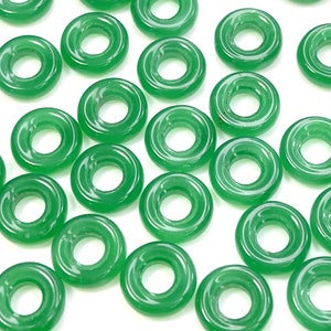 May include: A collection of green jade donut beads. The beads are smooth and polished, with a hole in the center. They are perfect for making jewelry or other crafts.