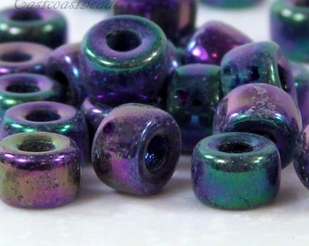 May include: A close-up of a pile of iridescent purple and green glass beads. The beads are small and round, with a hole in the center. They have a metallic sheen and are perfect for jewelry making.