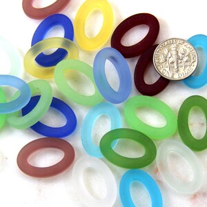 May include: Assortment of oval-shaped glass beads in various colors, including blue, green, red, yellow, and white. The beads are frosted and have a smooth, polished finish.