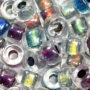 May include: A close-up of a pile of iridescent glass beads. The beads are clear with a variety of colors, including purple, blue, green, and gold. The beads are all about the same size and have a hole in the center.