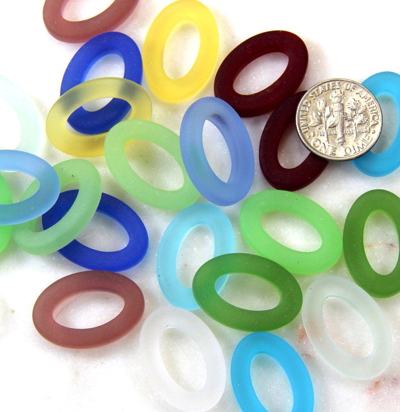 May include: Assortment of oval-shaped glass beads in various colors, including blue, green, yellow, red, and white. The beads are frosted and have a smooth, polished finish. The beads are approximately the size of a US dime.