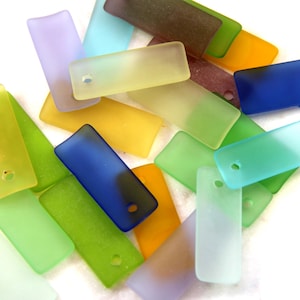 Puede incluir: Surtido de cuentas rectangulares de vidrio esmerilado en varios colores, incluyendo azul, verde, amarillo, morado y marrón. Cada cuenta tiene un pequeño agujero para enhebrar.