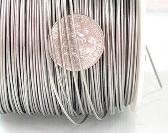 May include: A spool of silver-coloured wire with a 10 pence coin for scale. The wire is wound tightly around the spool.