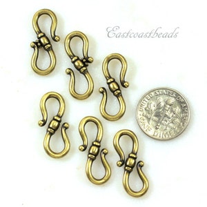May include: Six antique gold-toned metal lobster clasps, each with a decorative detail, shown next to a US dime for size comparison.