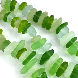 Puede incluir: Una hebra de cuentas de vidrio verde y blanco. Las cuentas son de forma ovalada y tienen un acabado liso y pulido.