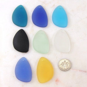May include: Nine glass teardrop-shaped pendants in various colors, including blue, green, yellow, black, and white. The pendants have a hole at the top for stringing.