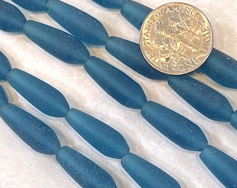 May include: A strand of teal blue glass beads, each bead is oval shaped and has a frosted finish. The beads are arranged in rows and are approximately the size of a US dime.