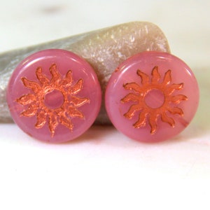 May include: Two pink glass round beads with a copper sun design.