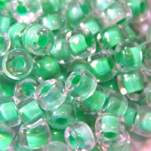 May include: A close-up of a pile of small, round, transparent plastic beads with a light green color. The beads have a hole in the center for stringing.
