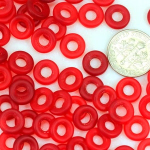 May include: A large quantity of red glass beads in the shape of a donut. The beads are translucent and have a glossy finish. A US dime is included for scale.