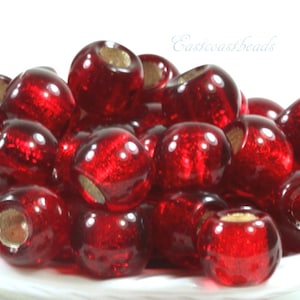 May include: A close-up of a pile of red glass beads with a hole in the center of each bead. The beads are round and have a shiny, glossy finish.
