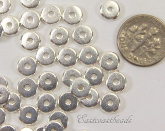 May include: A pile of silver-toned metal spacer beads, each with a round hole in the center. The beads are approximately the size of a US dime.