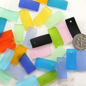 May include: Assortment of colorful frosted glass rectangle beads with a hole in the center. The beads are various shades of blue, green, yellow, orange, pink, and black.