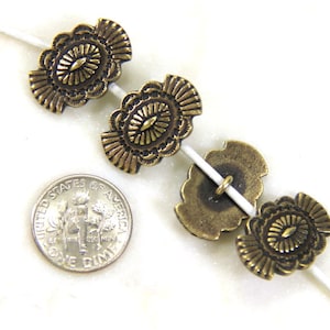 Pode incluir: Close-up de várias contas ovais de cor latão antigo com um design floral. As contas são enfiadas em um fio branco. Uma moeda de dez centavos dos EUA está incluída para comparação de tamanho. As contas têm uma superfície detalhada e texturizada.