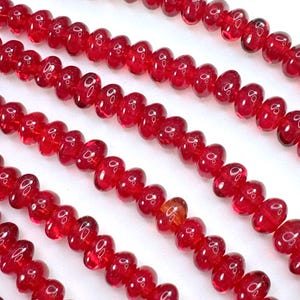 May include: A strand of bright red glass beads, each bead is shaped like a heart. The beads are strung on a clear thread and are arranged in a row.