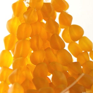 May include: Close-up of a strand of amber-colored, irregular-shaped beads. The beads are clustered together, creating a textured and visually appealing display. The background is a bright white.