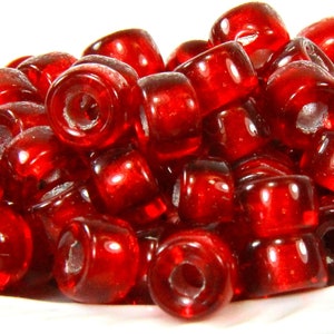 May include: A pile of translucent, cylindrical red beads. Each bead has a hole running through the center. The beads are glossy and reflect light, creating highlights. The beads are likely for jewelry making or crafts.