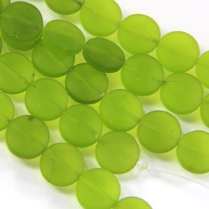 May include: Close-up of a collection of lime green, flat, round beads. The beads have a matte finish and a subtle line across the center. These beads are ideal for jewelry making and crafting projects.