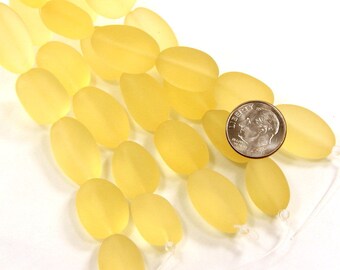 May include: A strand of oval-shaped, frosted yellow beads with a matte finish. A silver-coloured United States dime is placed on top of the beads to provide a visual scale reference for the size of each individual bead in the strand.