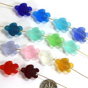 May include: Assortment of 12 glass sea turtle beads in various colors, including blue, green, pink, red, and orange. The beads are strung on gold wire.
