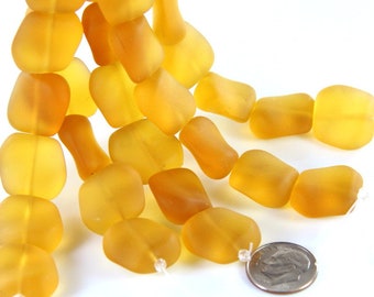 May include: A close-up of a strand of large, irregular, amber-coloured beads. The beads have a frosted appearance and are strung together. A coin is included for size comparison. The beads are a warm, golden hue.