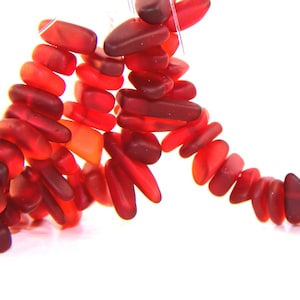 May include: A strand of red glass beads, each bead is a different shade of red and has a slightly irregular shape.