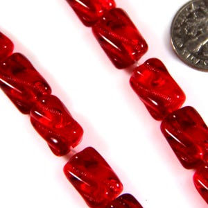 Könnte beinhalten: Eine Strähne roter Glasperlen mit einem gedrehten, strukturierten Design. Die Perlen sind quadratisch und haben eine glänzende Oberfläche.