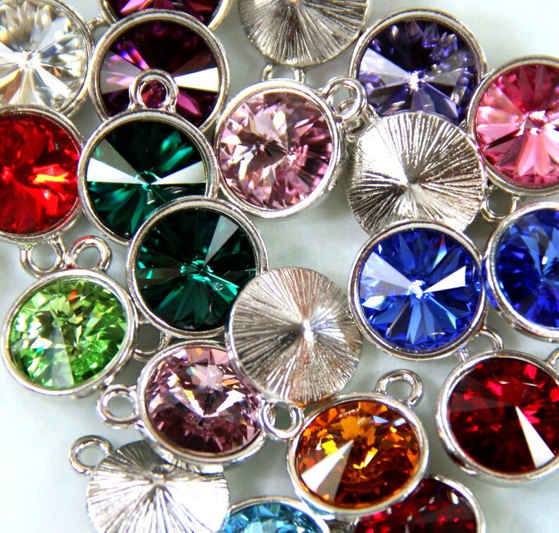 Puede incluir: Surtido de brillantes redondos de cristal de colores con engastes de metal plateado. Los brillantes son de varios colores, incluyendo rojo, verde, azul, rosa y morado.