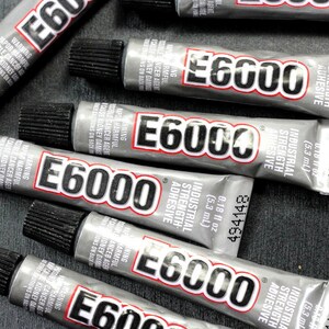 Op de afbeelding: Meerdere tubes E6000 industri&euml;le lijm met hoge sterkte, elke tube is gelabeld met de merknaam en productinformatie, inclusief de maat, 0,18 fl oz (5,3 ml).