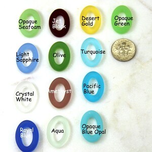 May include: Assortment of 14 oval-shaped glass beads in various colors, including opaque seafoam, jet black, desert gold, opaque green, light sapphire, turquoise, olive, amethyst, pacific blue, crystal white, royal blue, aqua, and opaque blue opal.