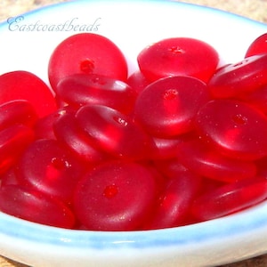 May include: A bowl filled with bright red, translucent, round beads with a hole in the center. The beads are arranged in a random pattern. The bowl is white with a blue rim.
