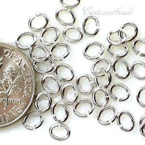 May include: A close-up of a pile of silver jump rings. The jump rings are oval shaped and are about the size of a US dime.