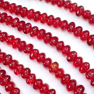 May include: A strand of bright red glass beads, each bead is shaped like a heart. The beads are strung on a clear thread and are arranged in a row.
