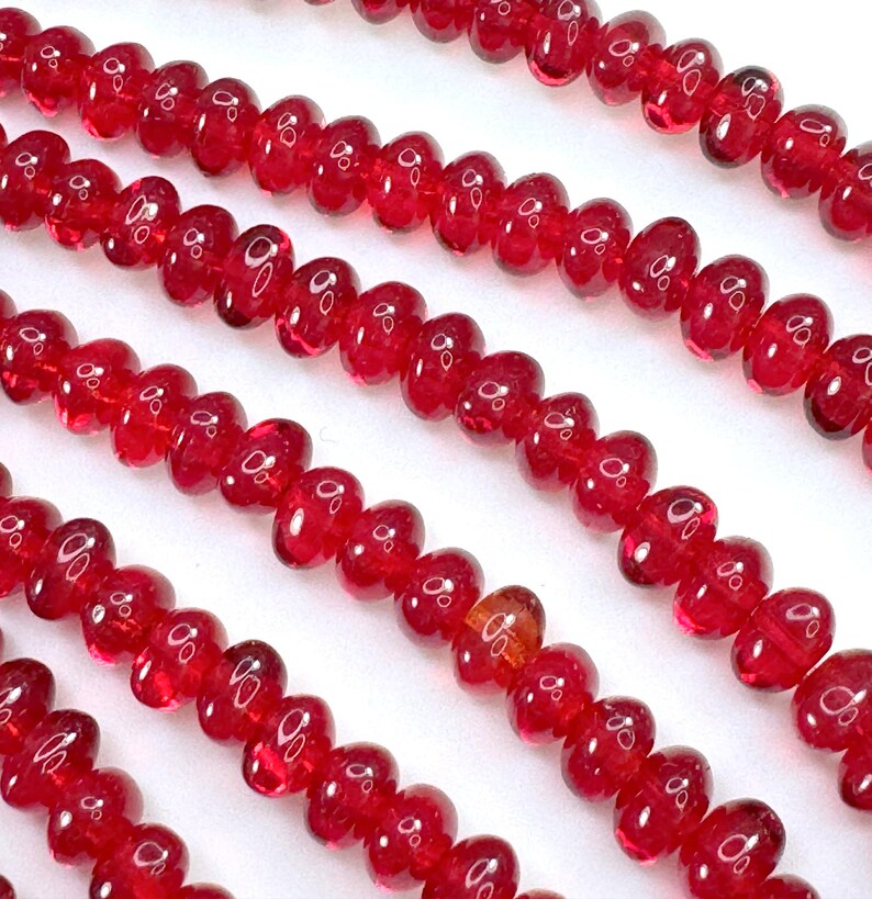May include: A strand of bright red glass beads, each bead is shaped like a heart. The beads are strung on a clear thread and are arranged in a row.