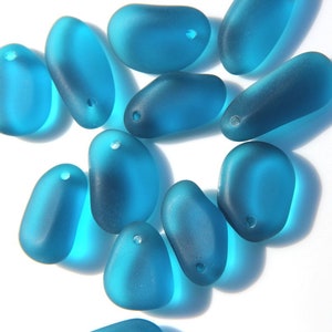 May include: A collection of teal blue glass beads, each with a small hole for stringing. The beads are smooth and have a slightly frosted finish.