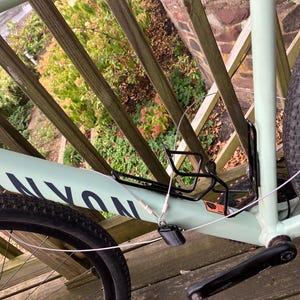 May include: A light green Canyon bicycle with a black tyre, black water bottle cage, and a silver cable lock. The bicycle is parked on a wooden deck.