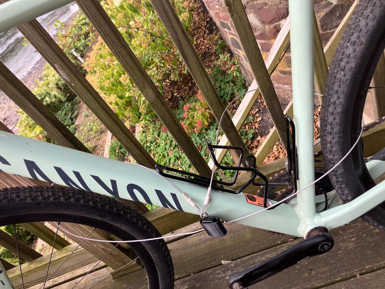 May include: A light green Canyon bicycle with a black tyre, black water bottle cage, and a silver cable lock. The bicycle is parked on a wooden deck.