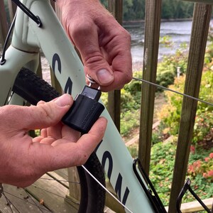May include: A black bike lock with a silver key attached to a bike frame. The lock is secured to a metal cable.